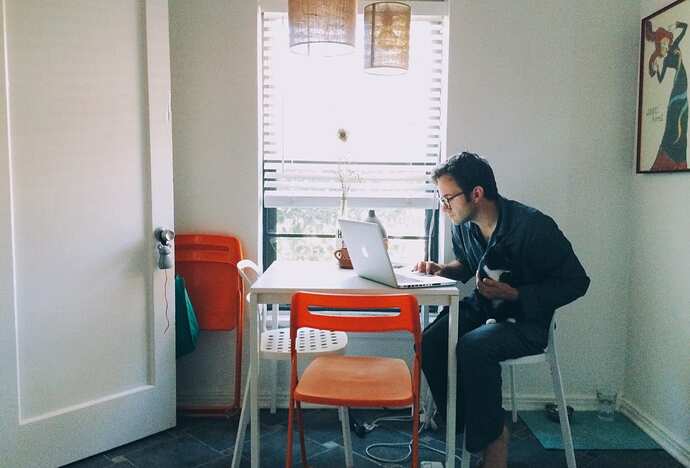 106439181-1584028212076a-man-wearing-pajamas-works-on-his-laptop-in-the-dining-room-while-petting-the-cat-in-his-lap_t20_3ezjxr